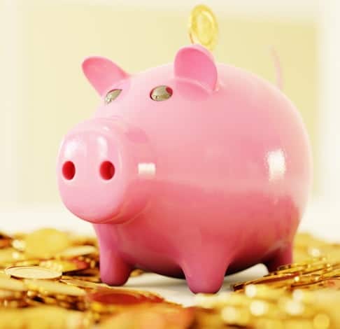 photo de tirelire en forme de cochon rose posé sur sol jonché de pièces d'argent